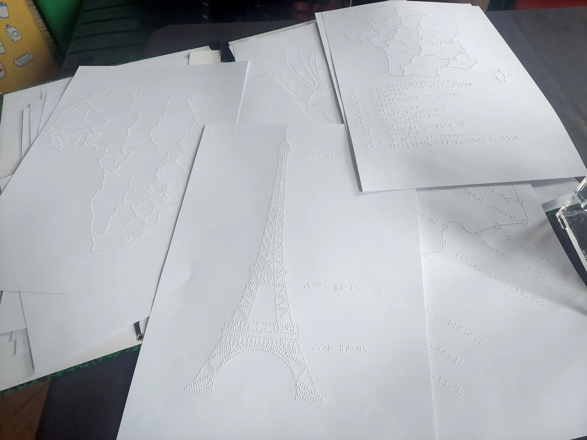 Des examples de documents produits sur une BrailleRAP qui mélange des graphiques avec des annotations en Braille. Une carte de France, la tour Eiffel, une carte d'Afrique. 