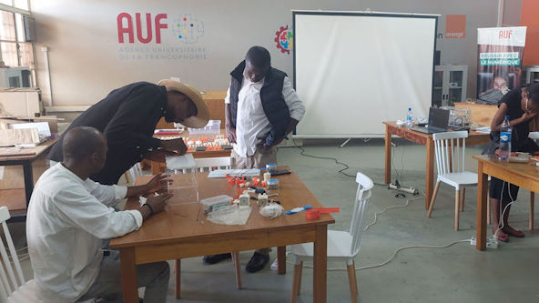 2 people observe a 3rd person performing an assembly operation on a BrailleRAP.